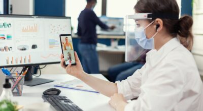 businesswoman-using-wireless-headphones-online-conference-smartphone-wearing-face-mask-workplace-multiethnic-coworkers-working-respecting-social-distance-business-global-pandem (1)