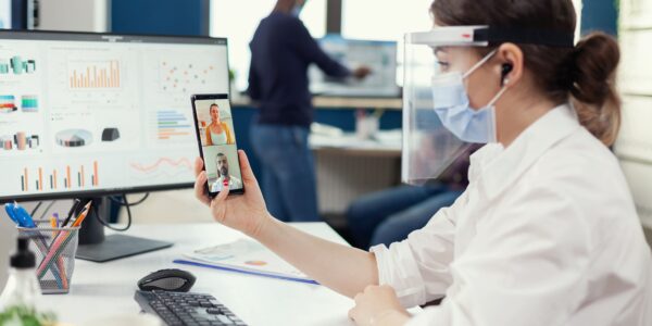 businesswoman-using-wireless-headphones-online-conference-smartphone-wearing-face-mask-workplace-multiethnic-coworkers-working-respecting-social-distance-business-global-pandem (1)